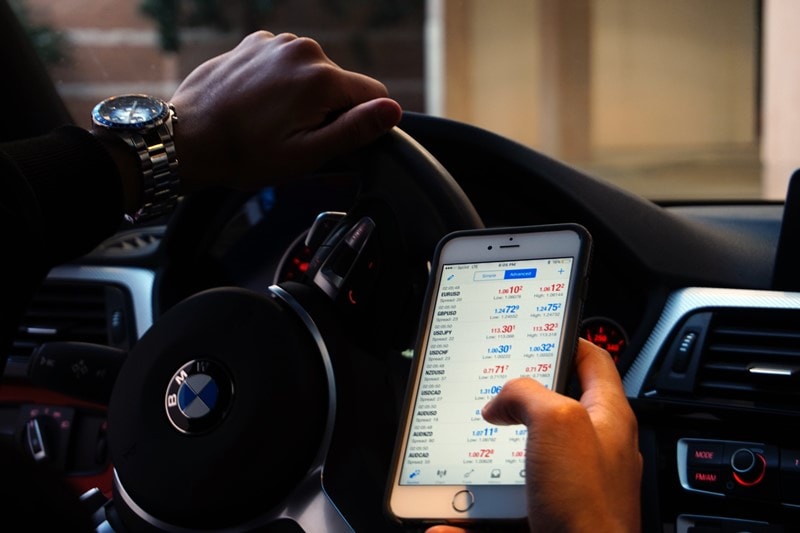 Mann im Auto prüft Aktienkurse auf dem Smartphone